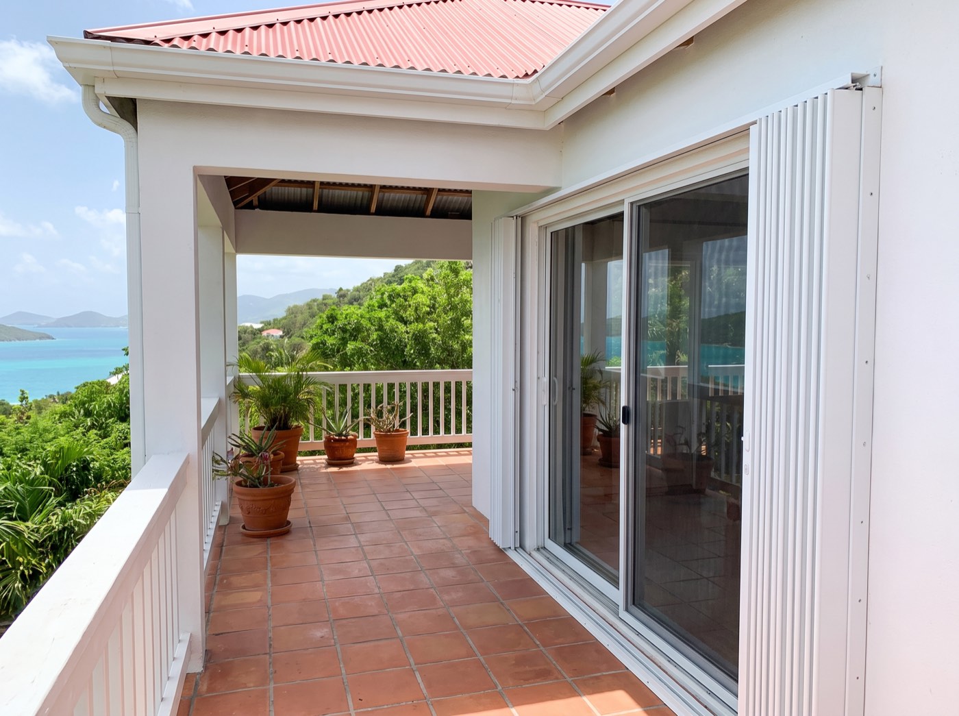 White accordion shutters folded back beside a sliding glass door on a Virgin Islands veranda overlooking a turquoise bay.